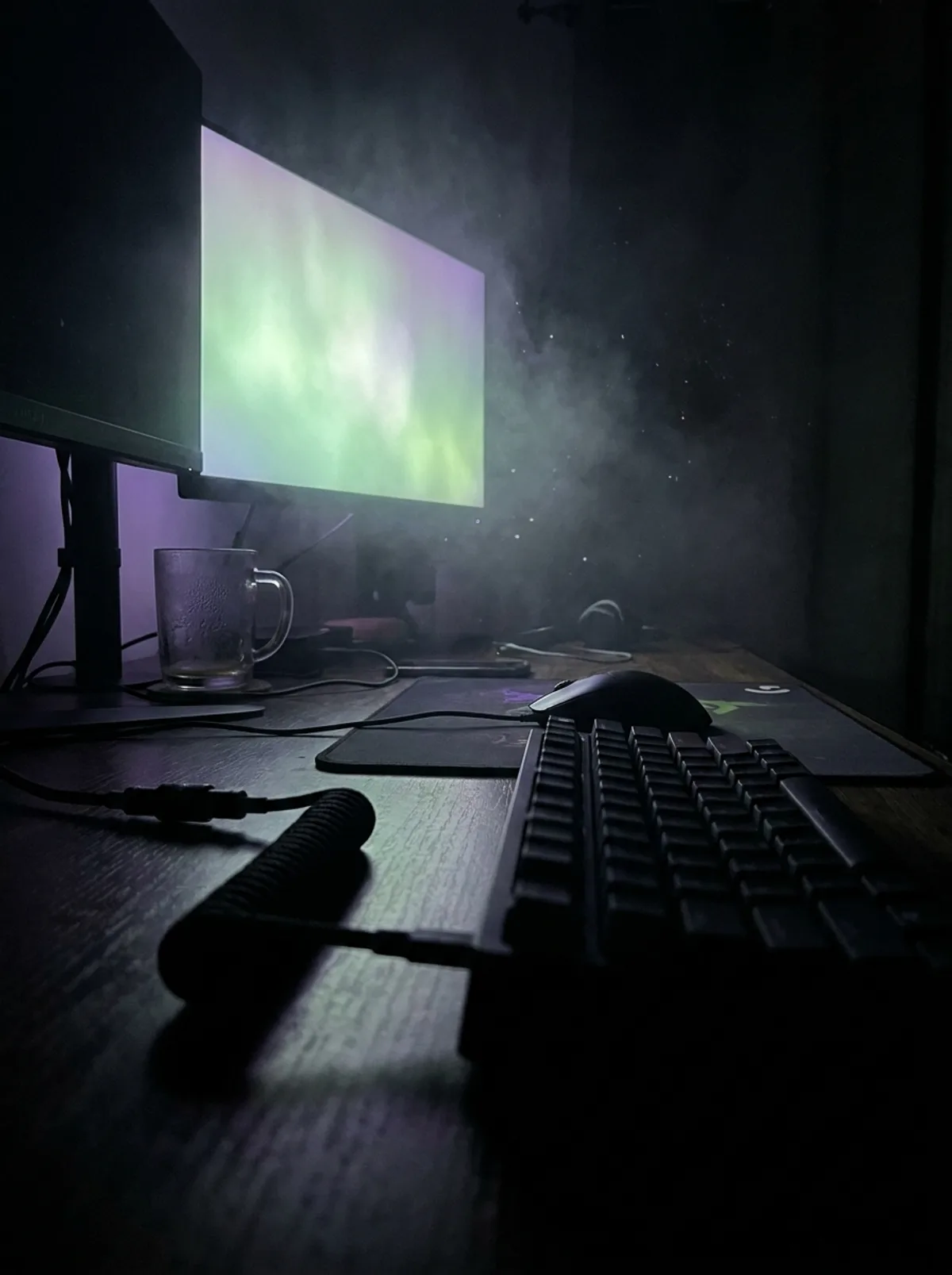 A dark desk at night, haze catching the green and violet glow of a screen